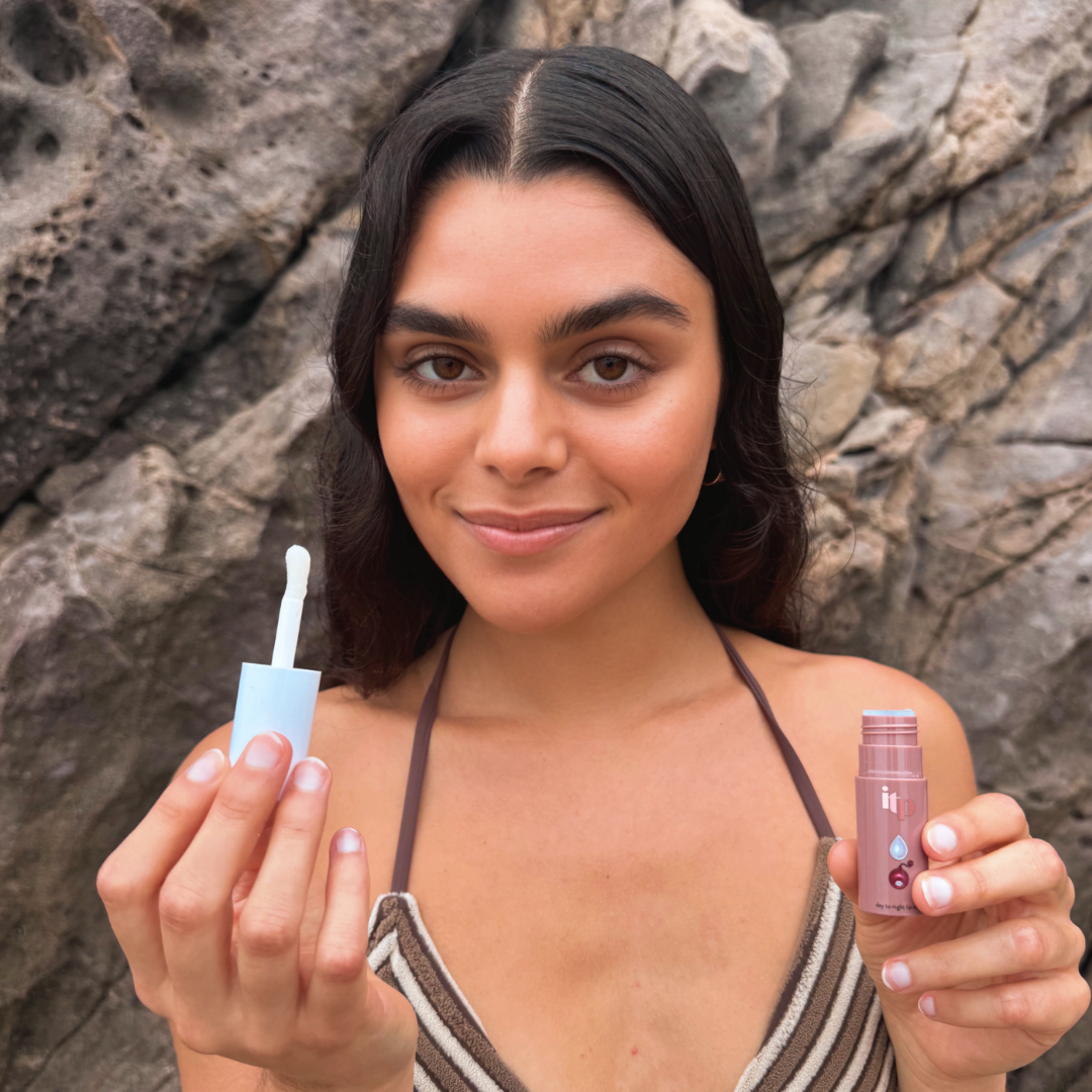 Woman holding two skincare products against a stone wall background